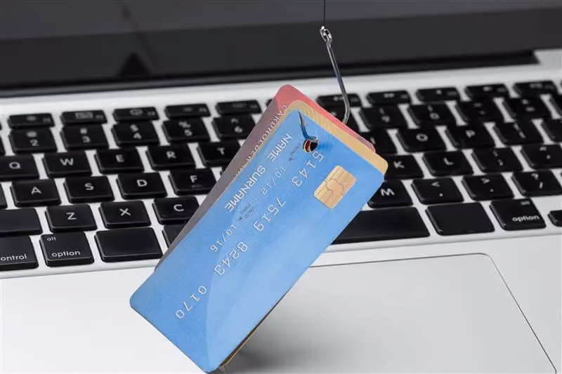 Credit card on a fishing hook over a keyboard, illustrating an email phishing attempt