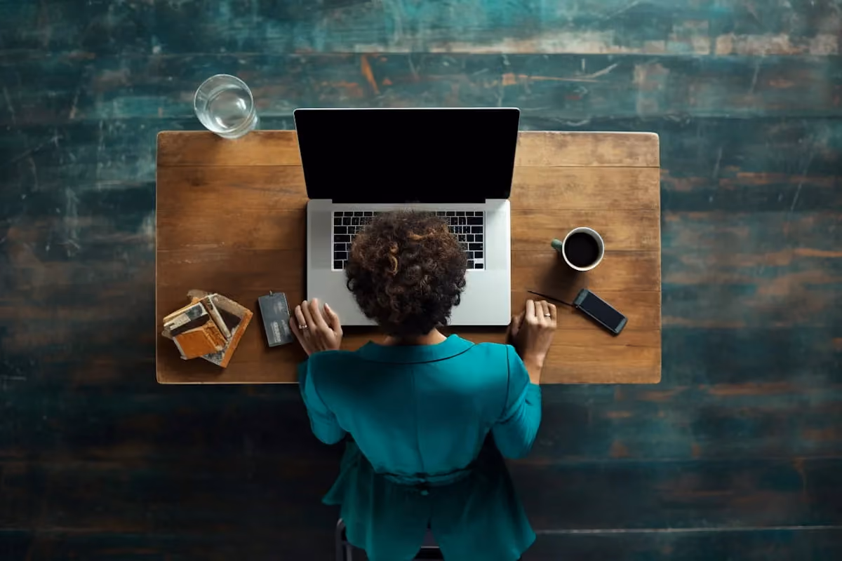 Overhead view of a person working on a laptop at a wooden desk